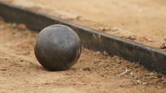 an old metal ball sitting on the ground next to a pipe in the dirt,