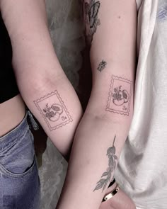 two people with tattoos on their arms holding onto each other's arm and both have postage stamps on them