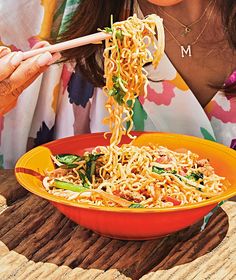 a woman is eating noodles with chopsticks