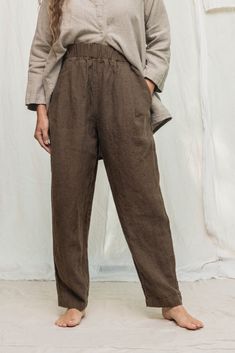 a woman standing in front of a white backdrop wearing brown pants and a gray shirt