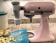 a pink mixer sitting on top of a kitchen counter next to cookies and doughnuts