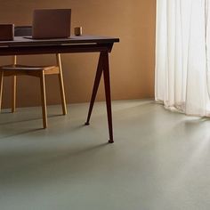 a laptop computer sitting on top of a wooden desk next to a chair and window