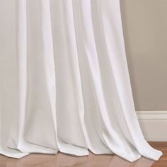 a white curtain hanging on the side of a wooden floor next to a window with curtains