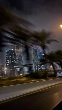 a city street at night with the lights on and trees blowing in the foreground