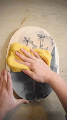 someone wiping down a plate with a yellow sponge on it and another hand reaching for the dust