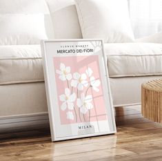 a white couch sitting next to a window with flowers in front of it on top of a hard wood floor