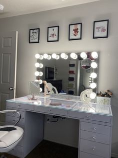 a white vanity with lights on it and a chair in front of the mirror that is lit up