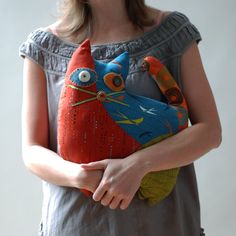 a woman is holding an orange and blue cat pillow in her hands while wearing a gray top