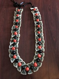 a necklace made out of dollar bills and red beads on a wooden floor with a black ribbon