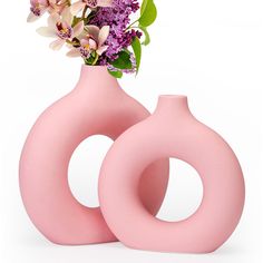 two pink vases with flowers in them on a white surface, one is shaped like the letter o