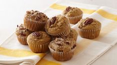 a bunch of muffins sitting on top of a yellow and white towel with pecans