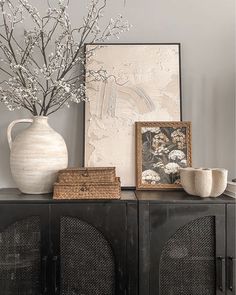 a white vase sitting on top of a wooden cabinet next to a painting and two baskets