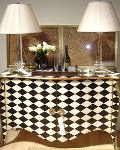 a black and white checkered buffet table with two lamps on it, next to a mirror