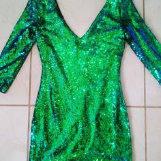 a green sequin dress laying on the floor next to a white tile wall and tiled floor