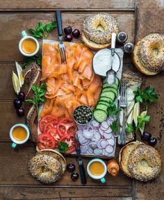 an assortment of food is laid out on a table with bread, olives, tomatoes, cucumbers and bagels