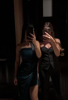 two women in dresses are taking pictures with their cell phones and one is wearing a black dress