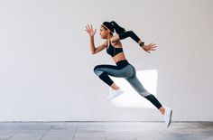 a woman is jumping in the air with her arms outstretched by an empty wall and floor