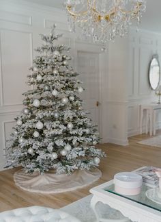 a white christmas tree in a living room next to a chandelier and mirror