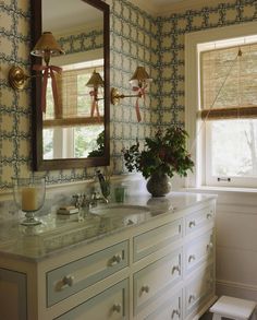 a bathroom with blue and white wallpaper, vanity mirror and vase filled with flowers