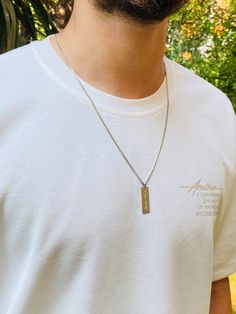 a man wearing a white t - shirt and a necklace with a tag on it