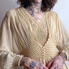 a woman with tattoos on her arms and chest is posing for the camera while wearing a beige dress