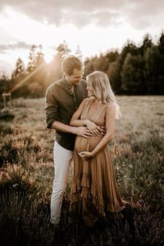 a pregnant couple standing in a field at sunset