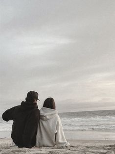 two people sitting on the beach looking out at the ocean