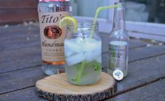 there is a drink with ice and lemon in it on the wooden table next to two bottles