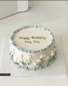 a birthday cake with white flowers and green writing on the top is sitting on a table