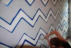 a woman is painting a wall with blue and white lines on it in the bathroom