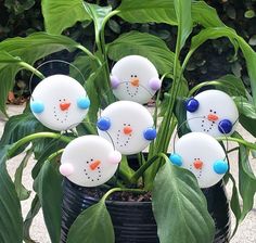 a potted plant with snowmen sitting on it's sides and green leaves in the background