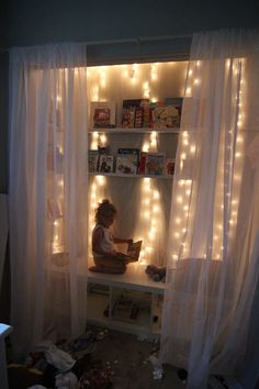 a child sitting on a shelf in front of a window with fairy lights