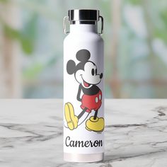 a stainless steel water bottle with a cartoon mickey mouse on the front and bottom, sitting on a marble surface