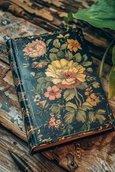 an old book is sitting on a wooden table next to a pen and flower pot