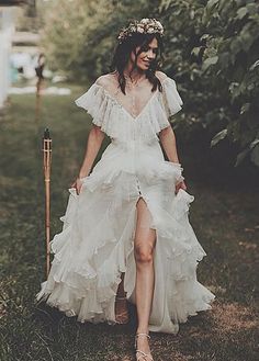 a woman in a white dress is walking through the grass with a stick and flower crown on her head