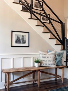 a wooden bench sitting under a stair case next to a wall with pictures on it