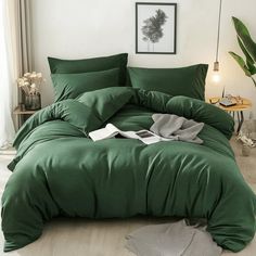 a bed with green sheets and pillows in a room next to a plant on the floor