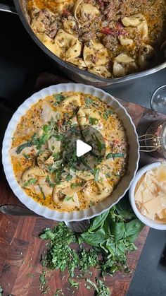 two pans filled with food sitting on top of a wooden table next to other dishes