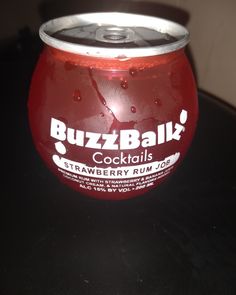 a can of buzzball cocktail sits on a black table in front of a wall