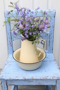 a white vase with purple flowers in it sitting on a blue chair