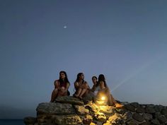 three women sitting on rocks at the edge of the water with lights in their hands