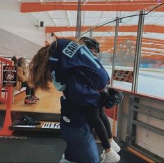 two girls are playing ice hockey on an indoor rink while one girl is holding onto the back of another girl