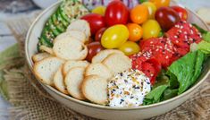 a close up of a bowl of food with tomatoes, lettuce and crackers