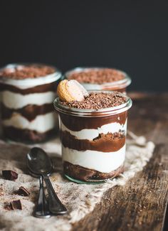 three desserts in small glass jars with spoons on the table next to them