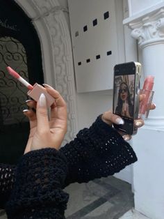 a woman taking a selfie with her cell phone while holding two lipstick sticks in front of her face