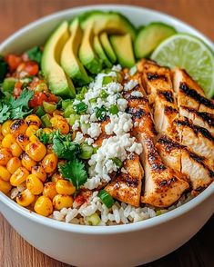 a white bowl filled with chicken, rice and avocado on top of a wooden table