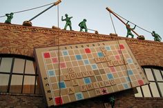 a scrabble board on the side of a brick building with people standing on top