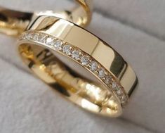 two gold wedding rings sitting on top of each other with white diamonds in the middle