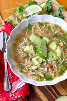 a bowl of soup with avocado, cilantro and lime on the side