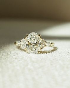 a three stone diamond ring sitting on top of a white cloth covered floor with sunlight shining through the window